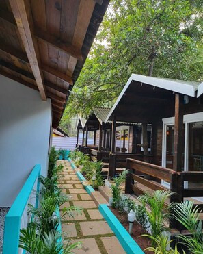 Un espacio al aire libre cubierto con bancos de madera y plantas en macetas, que conduce a un edificio con grandes ventanales.