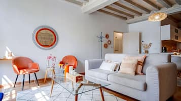 Un salon moderne avec un canapé gris, deux fauteuils orange, une table basse en verre et un tapis à motifs.