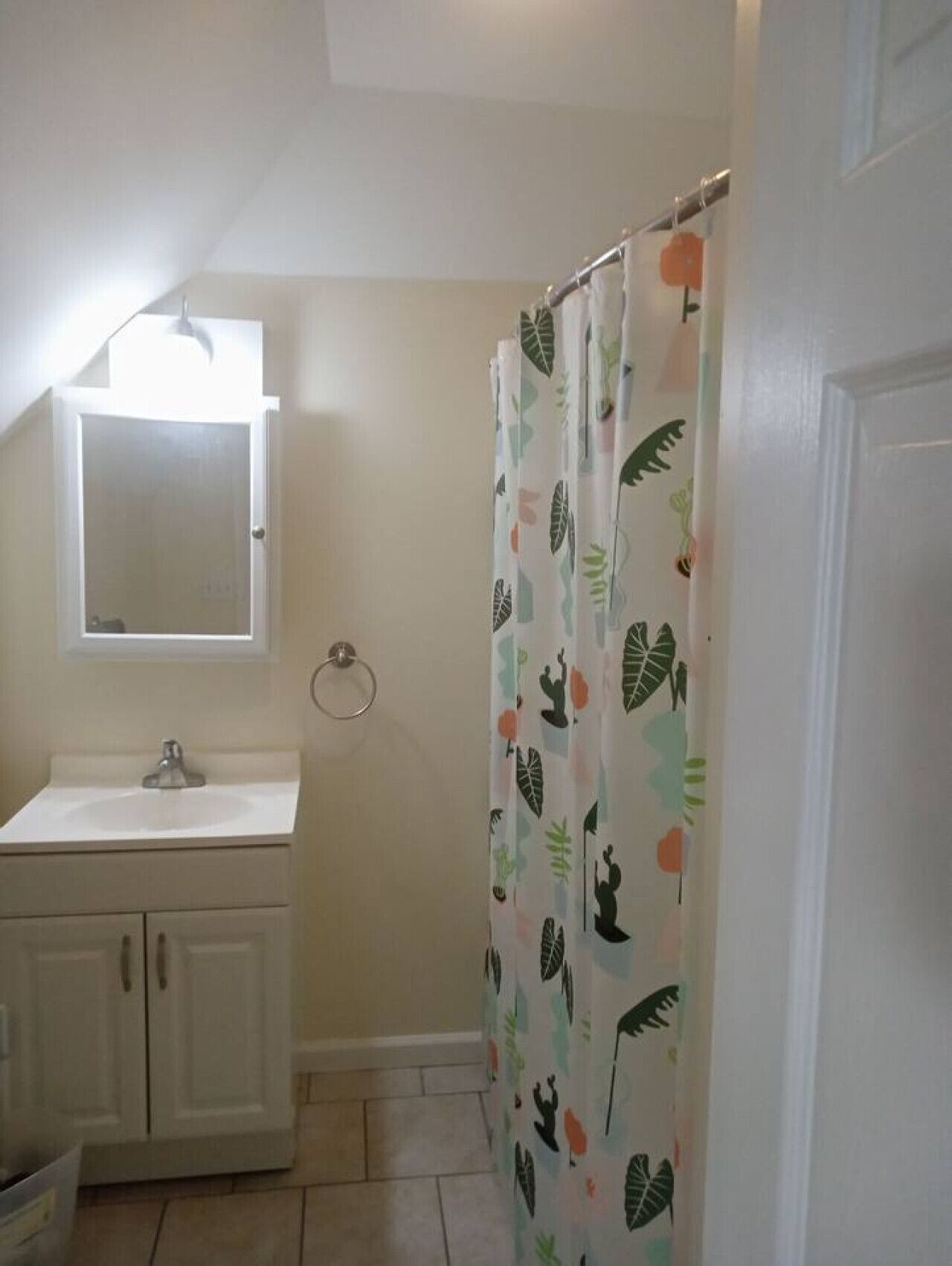 Un baño con lavamanos blanco, un espejo encima y cortina de ducha con estampado de hojas.