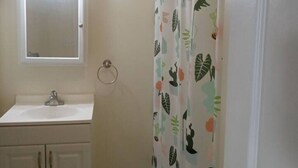 A bathroom with a white sink, a mirror above it, and a shower curtain with a leaf pattern. - a nice one bedroom free parking (Schenectady)
