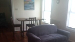 A living room with a gray sofa, wooden flooring, a dining table with chairs, and a painting on the wall. - a nice one bedroom free parking (Schenectady)