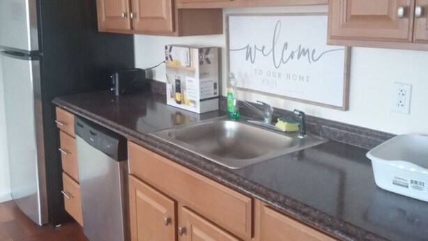A kitchen with wooden cabinets, a stainless steel refrigerator, a dishwasher, and a welcome sign on the wall. - a nice one bedroom free parking (Schenectady)