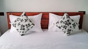 Un lit avec une tête de lit en bois, deux oreillers blancs ornés de motifs floraux noirs et un couvre-lit blanc uni.