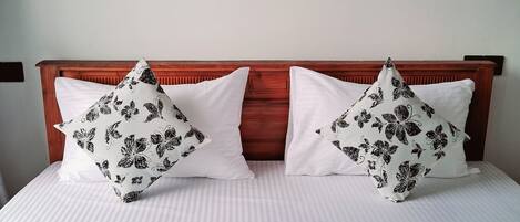 A bed with a wooden headboard, two white pillows with black floral patterns, and a plain white bedspread.