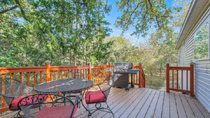 A wooden deck with a barbecue grill, a round table, and two chairs. - Secluded Country Home on 15 Acres with a BBQ and Upscale Kitchen. Close to COTA and the Airport. (Cedar Creek)