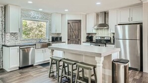 A modern kitchen with a large island, stainless steel appliances, and a stone backsplash. - Secluded Country Home on 15 Acres with a BBQ and Upscale Kitchen. Close to COTA and the Airport. (Cedar Creek)