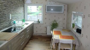Keittiössä on kiviseinä, ikkuna, pesuallas, ruokapöytä, jonka päällä on matto, ja seinälle asennettu televisio.