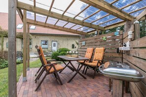 A covered patio with wooden furniture, a table, and a grill. - Apartment 'Alte Schule Pahlkrug' with Private Terrace, Private Garden and Wi-Fi (Linden)