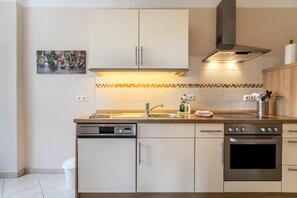 A modern kitchen with white cabinets, a dishwasher, an oven, a sink, and a tiled backsplash. - Apartment 'Alte Schule Pahlkrug' with Private Terrace, Private Garden and Wi-Fi (Linden)