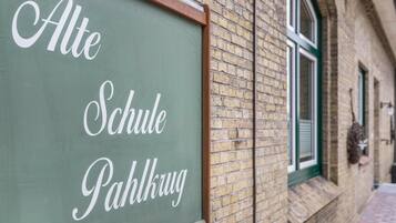 En tavle med 'Alte Schule Pahlkru' skrevet på, fastgjort til en murbygning med et vindue.