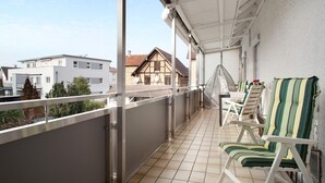 A balcony with a view of buildings, a covered area with chairs, and a tiled floor.