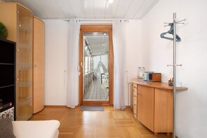 Habitación pequeña con un armario de madera, una mesita, un perchero y vistas a través de una puerta.