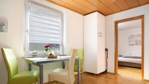 A compact room with a dining table, two chairs, a small kitchenette, and a bed.
