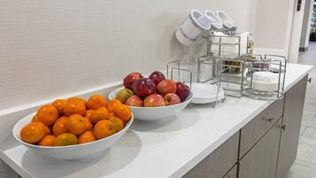 Una encimera de cocina con cuencos de naranjas y manzanas, un escurreplatos y una pared blanca.