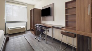 A hotel room with a bed, a desk with a chair, a TV mounted on the wall, and built-in wooden shelves. - MainStay Suites Chambersburg (Chambersburg)