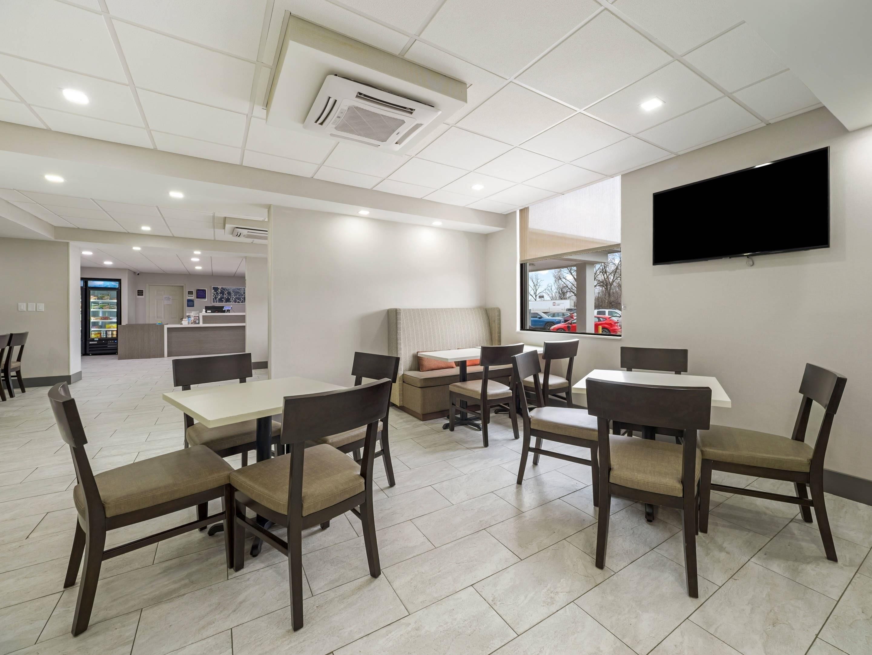 Un espace repas moderne avec des tables et des chaises, un téléviseur à écran plat fixé au mur et un distributeur automatique en arrière-plan.