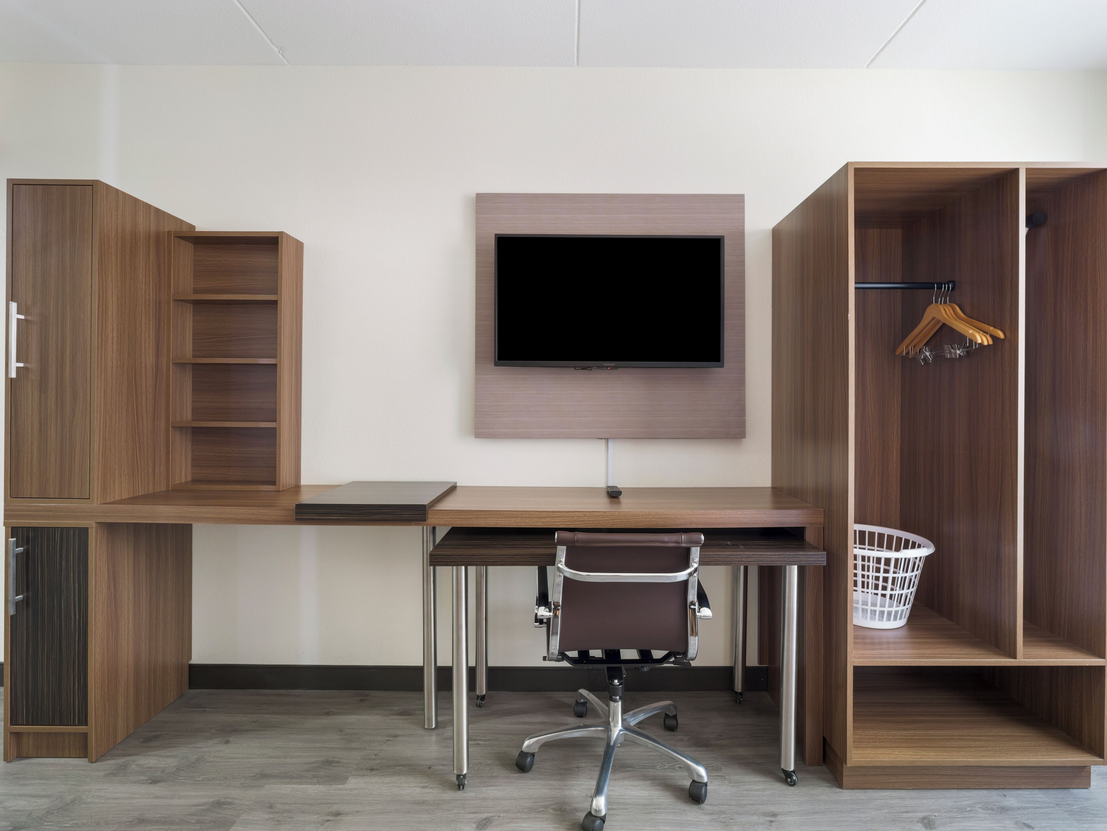 A modern office space with a desk, chair, TV, and built-in shelving.
