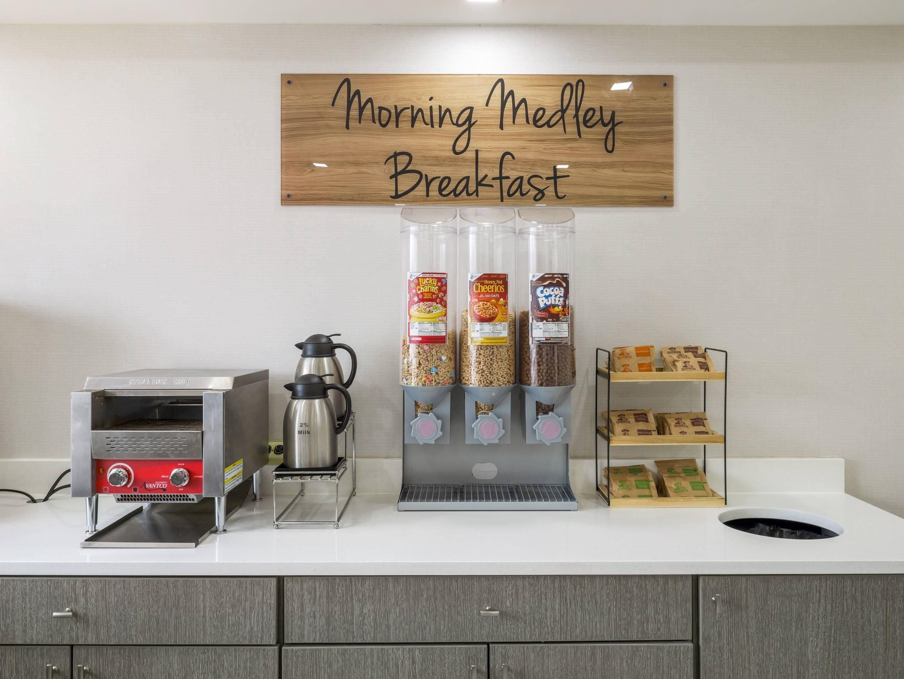 Una estación de desayuno con una cafetera, un letrero que dice 'Morning Medley Breakfast' y varios dispensadores de comida.