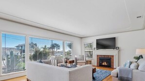 A spacious living room with large windows, a fireplace, and a flat-screen TV. - Opal Cliff Overlook (Santa Cruz)