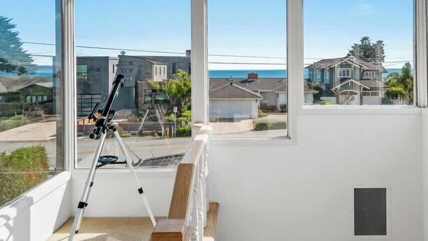 A room with large windows offering a view of a residential area and the sea. - Opal Cliff Overlook (Santa Cruz)
