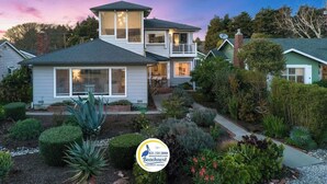 A two-story house with a balcony, surrounded by well-maintained gardens and a view of a body of water. - Opal Cliff Overlook (Santa Cruz)