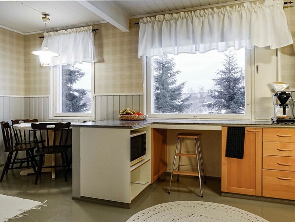 Une cuisine dotée d’un îlot central, de meubles en bois, d’un coin repas avec des chaises et de grandes fenêtres avec des rideaux.