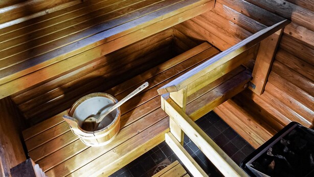 Una sauna con bancos de madera y un cubo de madera con una cuchara.