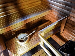 Un sauna avec des bancs en bois et un seau en bois accompagné d’une louche.
