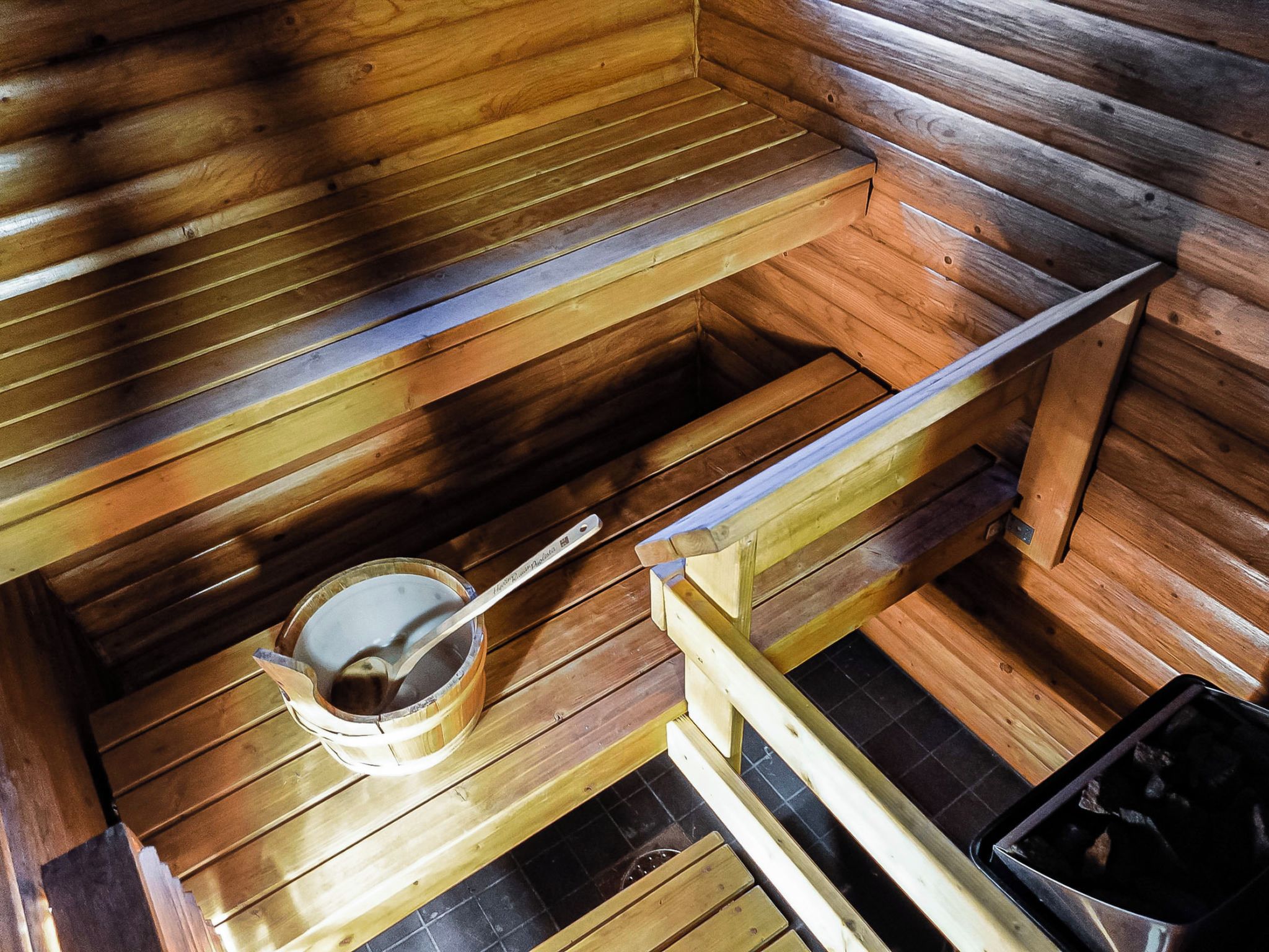 Sauna, jossa on puiset lauteet ja metallinen ämpäri sekä kauha.