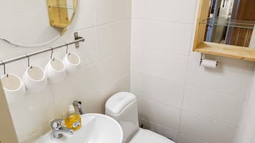 A bathroom with a white sink, a toilet, a mirror, and a shelf with cups.