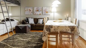 Un espacio habitable pequeño con una cama nido, un sofá, una mesa de comedor con sillas y una alfombra.