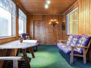 Ein Holzinterieur mit einem runden Tisch, zwei Stühlen, einem Sofa und einem Fenster mit Vorhängen.