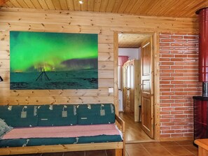 A wooden interior with a green and pink patterned sofa, a brick wall, and a painting of the Northern Lights.