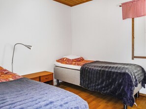 A simple room with two beds, a nightstand, a lamp, and a window with a checkered curtain.