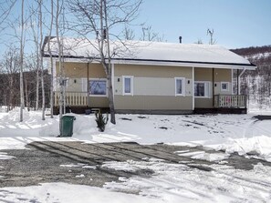 Une maison de plain-pied avec un porche à l’avant, une cheminée et un toit recouvert de neige.