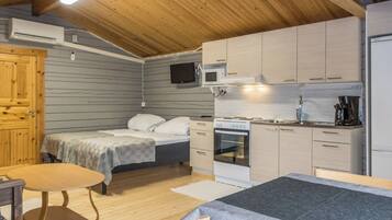 A compact room with a bed, a small table, a kitchenette, and a wooden ceiling.