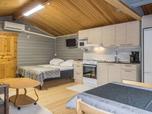 A compact room with a bed, a small table, a kitchenette, and a wooden ceiling.