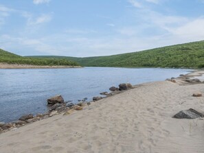 A riverbank with a sandy beach and scattered rocks.