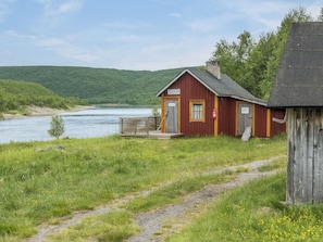 A small wooden building with a sauna and a water pump, situated by a river with a grassy path leading to it. - Nilla 3 by Interhome (Utsjoki)
