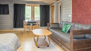 A cozy cabin interior with a wooden ceiling, a sofa with a green pillow, a dining table with chairs, and a view through a large window. - Nilla 3 by Interhome (Utsjoki)