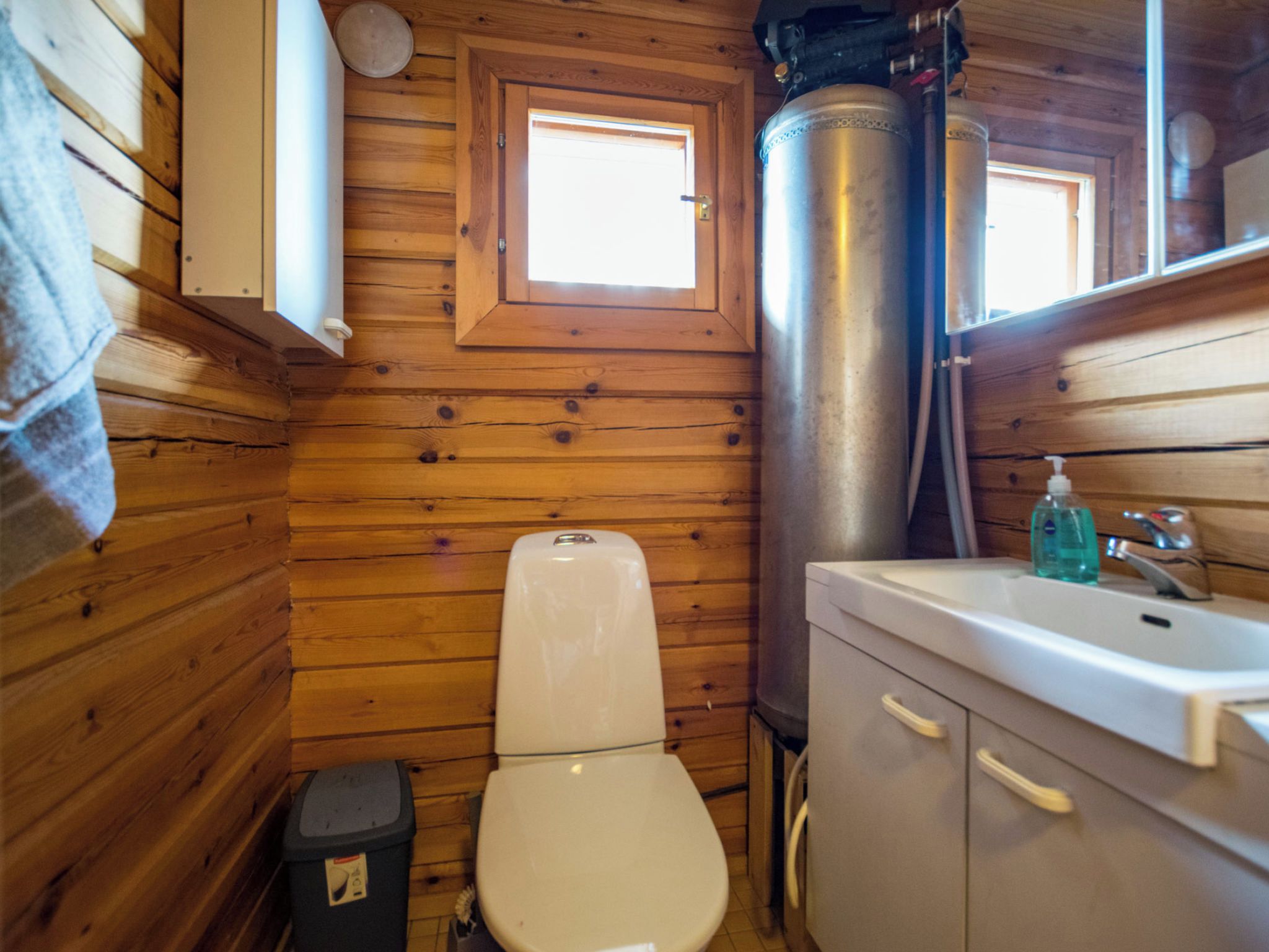 A compact wooden cabin bathroom with a toilet, sink, and a window.