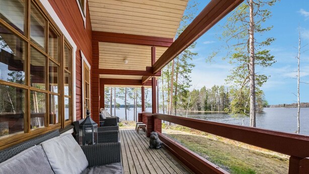 Een houten terras met een bank en stoelen, met uitzicht op een meer met bomen.
