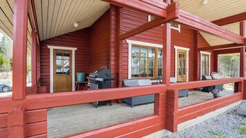 A wooden cabin with a porch, a grill, and a seating area.