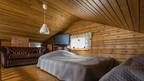 Een gezellige slaapkamer onder de pannen met houten wanden, een leren bank, een bed met een gewatteerde deken, een televisie en een raam met decoratieve gordijnen.