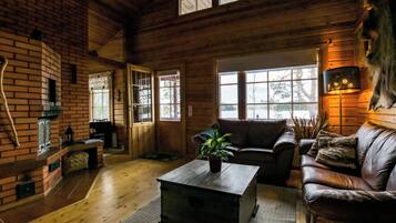 A cozy cabin interior with a wooden floor, a leather sofa, a coffee table, and a fireplace.