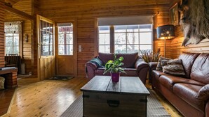 Een knus houten interieur met een leren bank, een houten salontafel en een groot raam dat voor natuurlijk licht zorgt.
