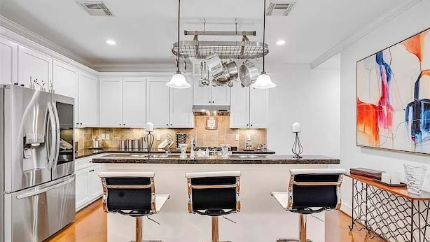 A modern kitchen with white cabinets, stainless steel appliances, and a central island with bar stools. - Luxurious 3BR 2.5BA Home with Hot Tub in Top Area (Houston)