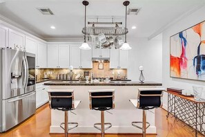 Una cocina moderna con gabinetes blancos, electrodomésticos de acero inoxidable y una isla central con taburetes de bar.