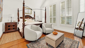 A spacious bedroom with a four-poster bed, two armchairs, a small ottoman, and a large mirror. - Luxurious 3BR 2.5BA Home with Hot Tub in Top Area (Houston)