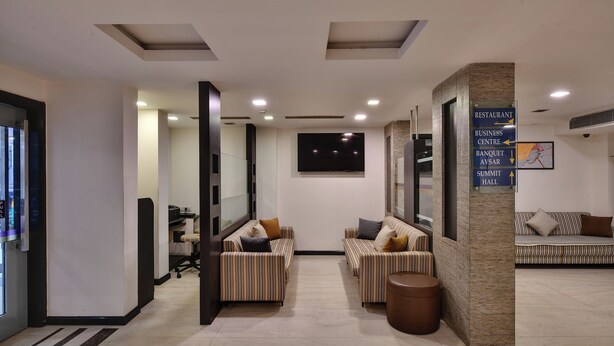 A modern lobby with striped sofas, a reception desk, and directional signage for amenities like the restaurant, business center, banquet, and summit hall. - Click Hotel Yuvraj (Surat)